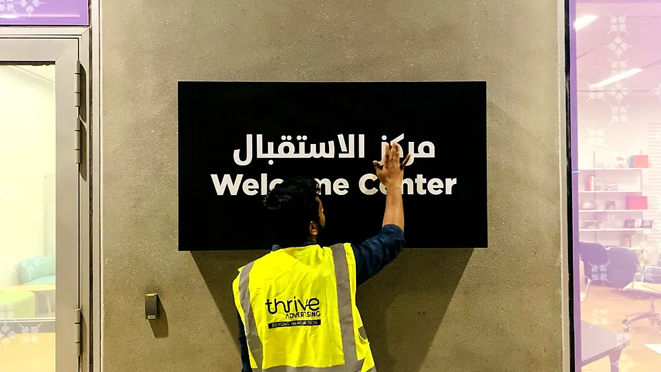 Thrive Advertising installer fitting a bilingual Welcome Center sign in Abu Dhabi